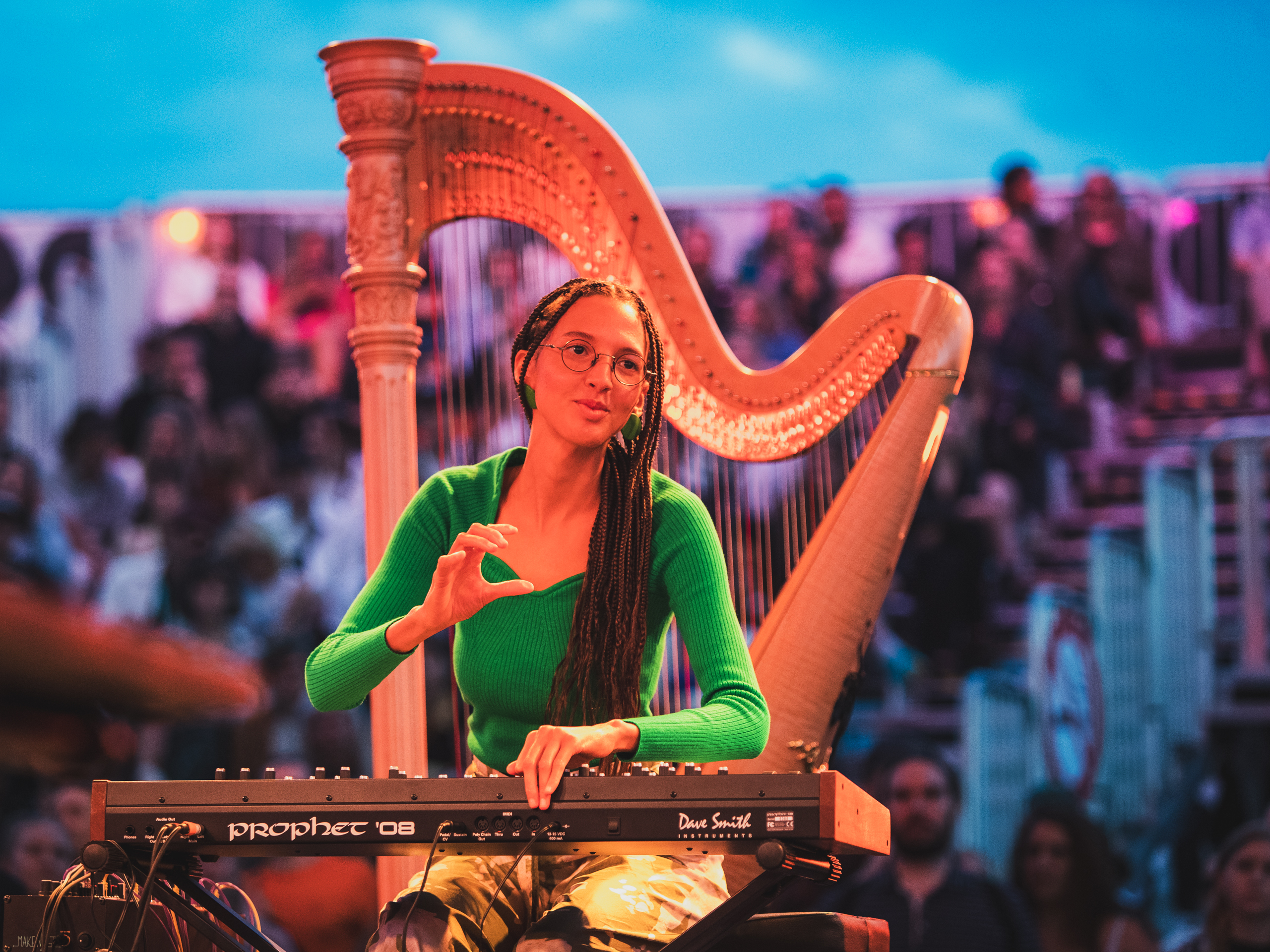 Nala Sinephro in performs at a piano in front of a giant harp
